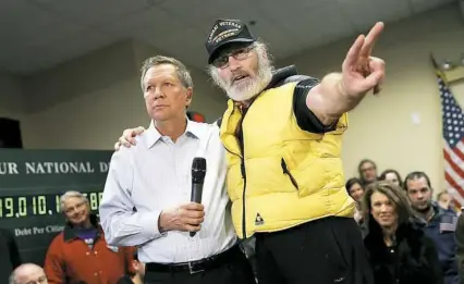  ?? Win McNamee/Getty Images ?? Vietnam veteran David AuCoin dra[es his arm around Republican presidenti­al candidate and Ohio Gov. John Kasich as he asks the candidate a question during a town hall Monday in Plaistow, N.H. Candidates were in a
last push for votes ahead of the...