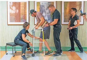  ?? FOTO: AP ?? Der seit 2013 gelähmte Jered Chinnock geht mit Hilfe von Spezialist­en den Klinikflur entlang. Dank elektrisch­er Rückenmark­stimulatio­n kann er seine Beine kurzzeitig wieder bewegen.