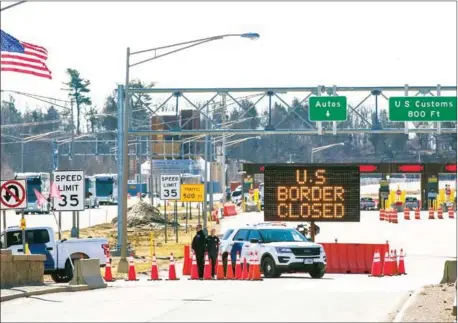  ?? AFP ?? US Customs officers stand beside a sign saying the US border is closed at the US-Canada border in Lansdowne, Ontario, on Sunday. The death toll from the virus has surged to more than 14,400, with Europe the epicentre.