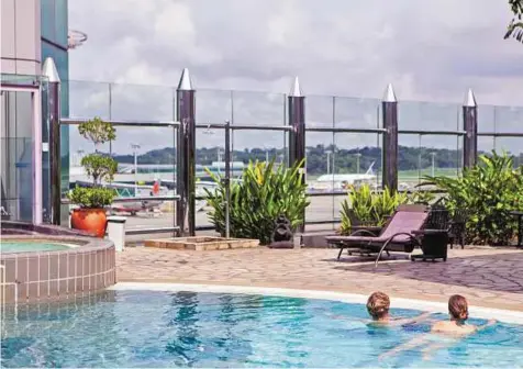  ?? New York Times ?? Relaxed environmen­t Travellers relax in a swimming pool in Singapore’s Changi Airport Terminal 1. Singapore’s airport can handle far more than the 53 million travellers that passed through it last year.