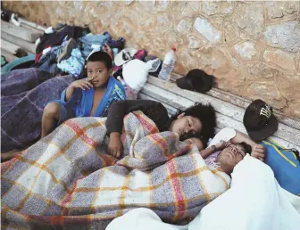  ?? AP PHOTOS ?? ‘DOING THINGS MILITARILY’: A boy sits awake, above right, as Central American migrants traveling to the U.S. sleep at a sports club in Mexico yesterday. A couple checks their cellphones, above left, before continuing the trek. President Trump said...