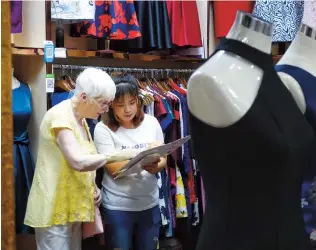  ??  ?? A shop assistant shows clothing styles to a foreign customer.