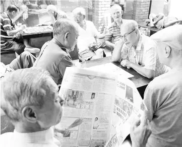  ??  ?? A man reads a newspaper as others play checkers in Singapore. — Reuters photo