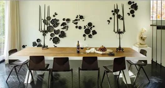  ?? PHOTOS: JOHN MCDONNELL/THE WASHINGTON POST ?? Darryl Carter designed this 11-foot dining table, made of 100-year-old oak and metal, which is surrounded by midcentury modern dining chairs. The black ceramic abstract art installati­on on the wall from French artist Sam Baron has both nature and whimsy: If you look closely, you will see lily pads, a lizard and a frog.
