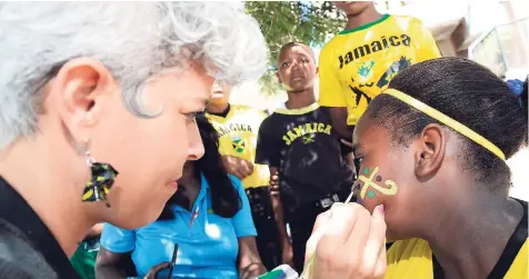  ??  ?? Natasha Parchment-Clarke, corporate trainer at Rainforest Seafoods, paints a Jamaican flag on the face of a student at the Rainforest Seafoods ‘Brain Food’ luncheon for the students at Iris Gelly Primary School during Jamaica Day recently.