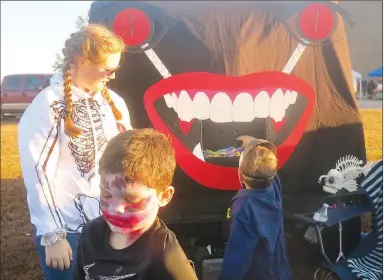  ?? Westside Eagle Observer/SUSAN HOLLAND ?? Elizabeth Becker, of Bella Vista, watches as a young trick-or-treater selects a candy treat from the giant mouth on the face at her family’s trunk during Saturday’s Gravette fall festival. The Becker family’s trunk was one of 17 offering candy and other prizes during the trunk-or-treat event. The festival also featured a petting zoo and games.