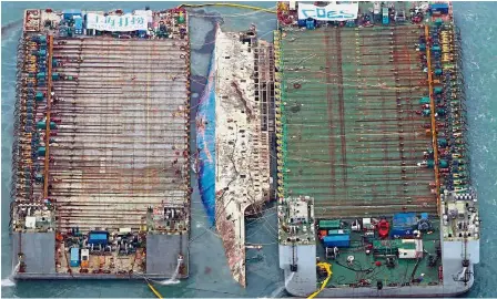  ??  ?? Long-awaited: An aerial view of part of the damaged Sewol ferry between two barges after being raised during a salvage operation at sea off the island of Jindo. (Below) A family member of a missing passenger crying during the operation. — AFP/Reuters