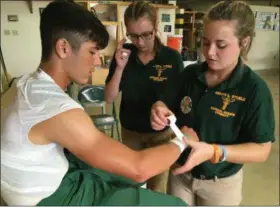  ?? RICHARD PAYERCHIN — THE MORNING JOURNAL ?? Amherst Steele High School junior Bailey Smith, 17, a student athletic aide, right, tapes the wrist of football player Liam Johnson as athletic aide Ava Kalonick-Gordon looks on before the Comets’ game against Berea-Midpark High School on Sept. 21.