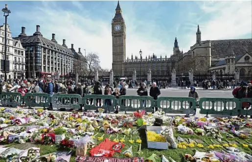  ??  ?? Keeping calm, carrying on: Passers-by looking at tributes in Parliament Square laid out for the victims of the Westminste­r attack. — AFP