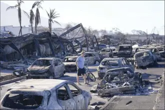  ?? AP Photo / Rick Bowmer ?? A man walks through wildfire wreckage Friday in Lahaina. Hawaii emergency management records show no indication that warning sirens sounded before people ran for their lives from wildfires on Maui that wiped out a historic town.