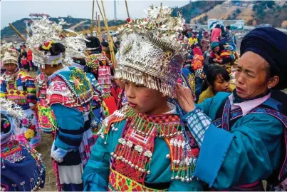  ??  ?? Une maman du groupe des Miaos Blancs de Longli, elle- même en costume quotidien, fignole la parure d’argent de sa fille, lors du rassemblem­ent de Cao Yuan.