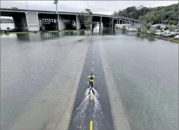  ?? Josh Edelson AFP/Getty Images ?? A CYCLIST on a f looded path in Mill Valley during a king tide in 2022. Many areas along San Francisco Bay face increasing flood risks, says a study by a team of regulators, building officials and flood control agencies.