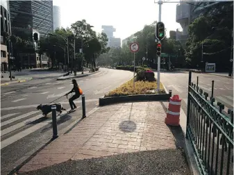  ??  ?? A young woman wearing a protective face mask controls her dog at a crossing of an empty Paseo de la Reforma in Mexico City. Because of the pandemic, millions of people in Mexico’s largest city have been staying home.