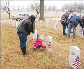  ?? Arkansas Democrat-Gazette/DAVE HUGHES ?? Addison Hale, 3, and her mother Elizabeth place a red flower on a grave at the Fort Smith National Cemetery Wednesday. The two were among about 25 who endured the drizzly morning to join Preston Sharp in honoring veterans. Sharp, 13, of Redding, Calif., travels the nation advocating the placement of flags and flowers at national cemeteries to honor veterans every day, not just on holidays. Sharp was recognized by President Donald Trump at his State of the Union address for his efforts to honor veterans.