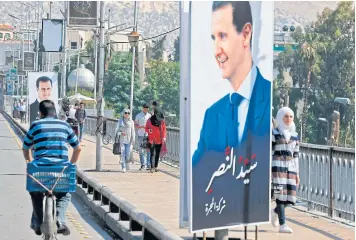  ?? AFP ?? People walk near a portrait of Syrian President Bashar al-Assad hanging in a street in the Syrian capital of Damascus yesterday.