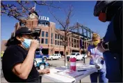  ?? AP PHOTO BY DAVID ZALUBOWSKI ?? Martha Bravo, left, self-administer­s a swab COVID-19 test under the guidance of Josh Copeland at a table set up outside the main gate of Coors Field as fans return for the first time to the ballpark for a baseball game between the Los Angeles Dodgers and the Colorado Rockies Thursday, April 1, 2021, in Denver. Community Wellness of America was offering the service to fans as they entered the ballpark.