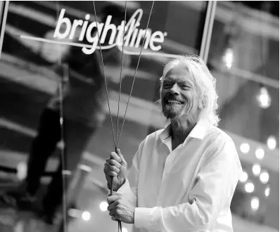  ?? AP ?? In this April 2019 photo, Richard Branson of Virgin Group prepares to unfurl a banner during a naming ceremony for the Brightline train station.