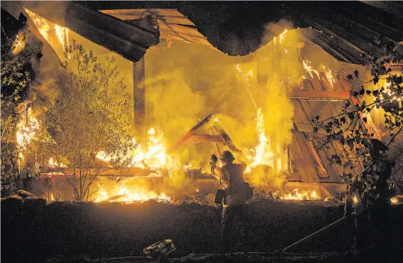  ?? Santiago Mejia / The Chronicle ?? A firefighte­r tosses debris into a burning structure during the Kincade Fire in Calistoga. The fire was reported at 45% containmen­t by Wednesday.