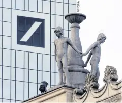  ??  ?? Figures of a statue ensemble at the roof of the Old Opera building in Frankfurt, with the Deutsche Bank building and signage on background on Wednesday.