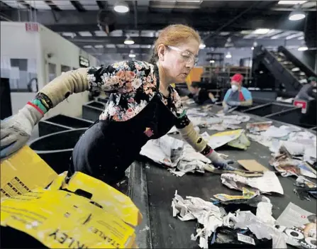  ?? Photograph­s by Carolyn Cole Los Angeles Times ?? A WORKER separates plastic bags and cardboard on a conveyor belt at the Athens Services Material Recovery Facility in Sun Valley.