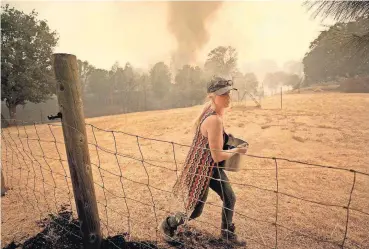  ?? [KENT PORTER/THE PRESS DEMOCRAT VIA THE ASSOCIATED PRESS] ?? Crystal Easter uses a pot of water to put out spot fires around her home, as her neighbor’s home burns to the ground in the background Monday in Spring Valley, Calif.