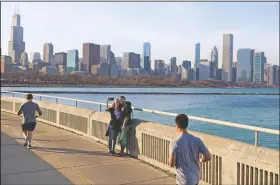  ?? (File Photo/AP/Shafkat Anowar) ?? A couple poses for a selfie March 9 as joggers pass by along Lake Michigan at Lakefront Trail in Chicago.