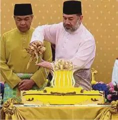  ??  ?? SULTAN Muhammad V diiringi Ahmad Zahid (kiri) memotong kek pada Majlis Santapan Teh Diraja sempena sambutan Hari Keputeraan Seri Paduka.