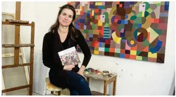  ??  ?? Gabrielle Thierry pose ici avec son livre devant sa dernière oeuvre, Le monde coloré des musiciens.