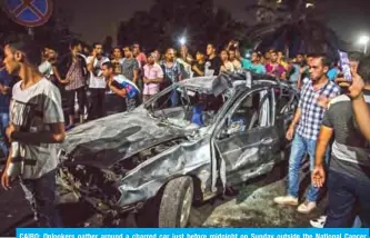  ??  ?? CAIRO: Onlookers gather around a charred car just before midnight on Sunday outside the National Cancer Institute in the Egyptian capital.