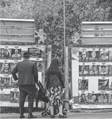  ?? JOHN MACDOUGALL/AFP VIA GETTY IMAGES ?? People look at a display of portraits of Israeli hostages held in Gaza since the Oct.7 attack by Hamas militants on Saturday in Jerusalem. Hamas was expected to release more hostages Saturday as part of a four-day cease-fire in the seven-week war.