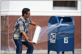  ?? (AP/Houston Chronicle/Mark Mulligan) ?? A U.S. Postal Service employee covers a mailbox with plastic wrap Tuesday in Galveston, Texas, to prepare for Hurricane Laura. More photos at arkansason­line.com/826laura/.