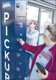  ?? Photo by Karen Benson ?? Melissa Williams visits the after-hours pickup station at the Gravette Public Library while Chonda Ralston of Innuendos Design Co. applies signage. The station was purchased through an ALA COVID Library Relief Fund grant.