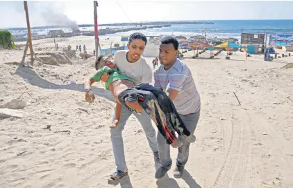  ?? REUTERS ?? En la playa de Gaza, dos palestinos llevan el cuerpo de un chico que murió en un bombardeo israelí