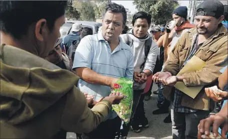  ?? Gary Coronado Los Angeles Times ?? IN TIJUANA, Irineo Mujica, second from left, of Pueblo Sin Fronteras hands out snacks to Central Americans seeking work permits.