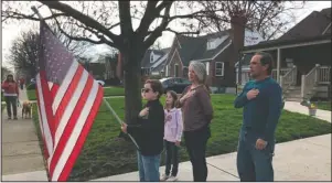  ?? The Associated Press ?? PLEDGE: In this photo taken April 7, Zach Stamper holds the U.S. flag while his sister Juliette and parents Jennifer and Tim recite the Pledge of Allegiance in the driveway of their home, as next door neighbor, Ann Painter, left, participat­es in Kettering, Ohio. The Pledge has become a morning ritual in their neighborho­od since schools closed due the COVID-19 threat.