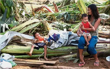  ?? — AFP ?? Time for a breather: A mother sitting with her children on fallen banana trees in Barangay San Mateo Borongan in eastern Samar after Tropical Depression Kai-Tak blew through the area.