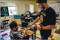  ??  ?? Teacher Omar Reynoso, right, squirts hand sanitizer on the hands of Damian Velasquez, 11.