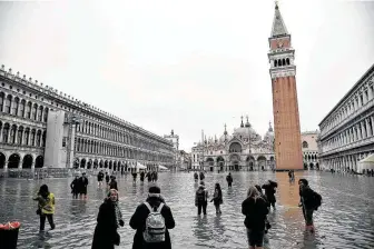  ?? Marco Bertorello /AFP / TNS ?? People walk across the flooded St. Mark’s square in Venice, with St. Mark’s basilica and the Bell Tower in the background, after an exceptiona­l overnight high tide.