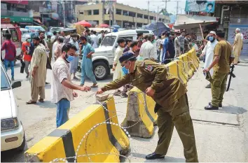  ?? AFP ?? Policemen put barbed wire as an market area is sealed in Rawalpindi. Pakistan is conducting less than 25,000 Covid-19 tests daily while a fortnight ago, the number was 30,000-35,000.