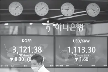  ?? ASSOCIATED PRESS ?? An employee of a bank walks by screens showing the Korea Composite Stock Price Index (KOSPI), left, and the foreign exchange rate between U.S. dollar and South Korean won at the foreign exchange dealing room in Seoul, South Korea. Asian shares mostly fell Thursday as caution set in over company earnings reports, recent choppy trading in technology stocks and prospects for more economic stimulus for a world battling a pandemic.