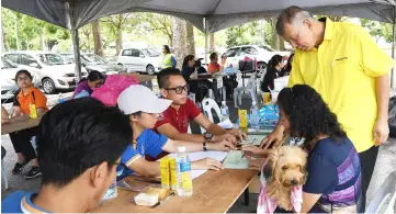  ??  ?? Ting (standing, right) helps a dog owner register her pet for vaccinatio­n at Miri Indoor Stadium.