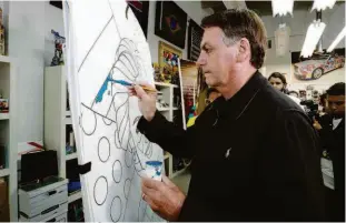  ?? Alan Santos/pr ?? O presidente Jair Bolsonaro pinta quadro feito por Romero Britto em homenagem à primeira-dama Michelle no estúdio do artista em Miami