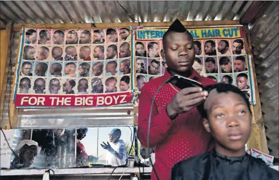  ??  ?? Persuasive: The barber shop is a great place to find a captive audience, giving volunteer Mpho Legofe (reflected in the mirror) enough time to convince an unsure voter that Bacs is the perfect choice