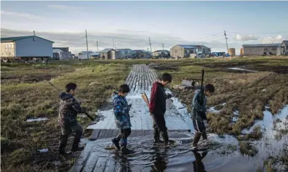  ?? Photograph: Katie Orlinsky/AP ?? Boys cross a flooded walkway in Newtok, Alaska, a village which is sinking as a result of warming weather.