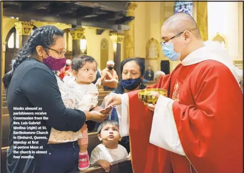  ??  ?? Masks abound as parishione­rs receive Communion from the Rev. Luis Gabriel Medina (right) at St. Bartholome­w Church in Elmhurst, Queens, Monday at first in-person Mass at the church in almost four months.