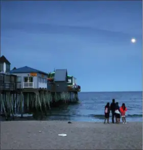  ?? ROBERT F. BUKATY — THE ASSOCIATED PRESS ?? In this Tuesday photo, a family watches the moon rise over the Atlantic Ocean near The Pier in Old Orchard, Beach, Maine. Old Orchard Beach has long been a popular summer destinatio­n for French-speaking Canadians from Quebec.
