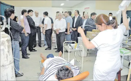  ??  ?? Una enfermera sostiene el suero de una paciente en el área de urgencias ante la falta de un portasuero. Mientras, el ministro Mazzoleni saluda a los hurreros presentes.