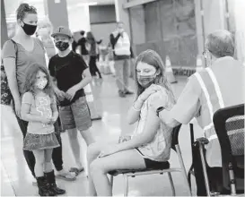  ?? DYLAN SLAGLE/BALTIMORE SUN MEDIA ?? Dr. Steve Grufferman administer­s a dose of the Pfizer Covid-19 vaccine to Mia O’Connor, 13, as her mother Jamie, and siblings Eve, 4, and Cole, 10, look on during a vaccinatio­n clinic in Westminste­r in May.