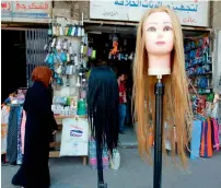  ?? AFP ?? A woman walks past wigs for sale outside a shop on Al Rasheed street, the oldest street in the Iraqi capital Baghdad, on Thursday. —