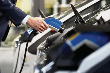  ??  ?? New technology: A man plugs a charger cable into Toyota’s i-Road electric vehicle in Tokyo. Toyota’s new electric car, to be built on an all-new platform, will use all-solid-state batteries. — Reuters